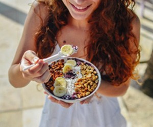 Woman smiling while eating smoothie bowl outside