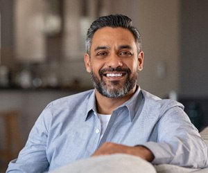 Man in blue shirt smiling while sitting on couch at home