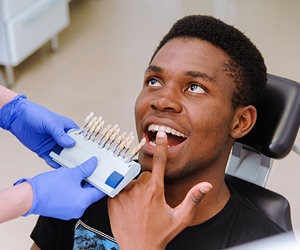 Young man’s smile compared with tooth color chart