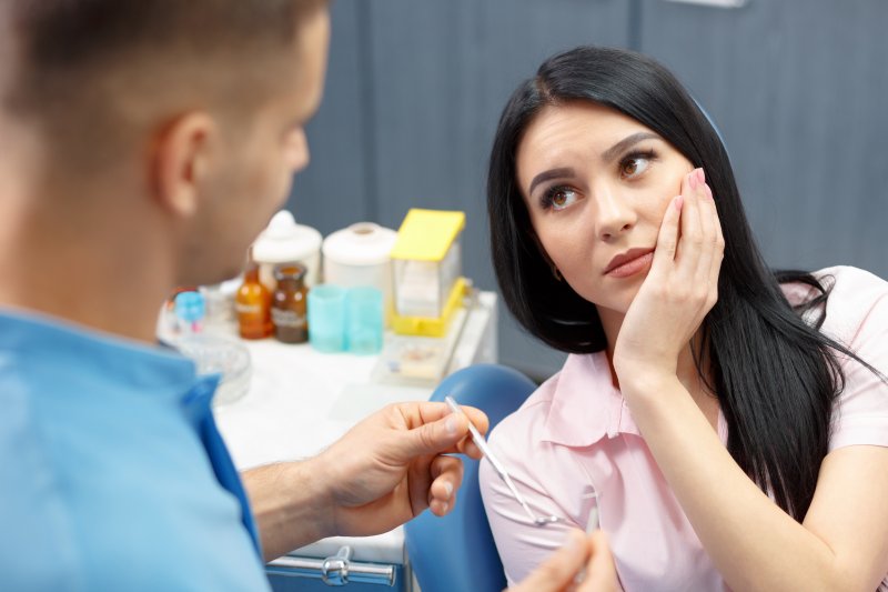 A woman holding her jaw at the dentist because she needs a root canal